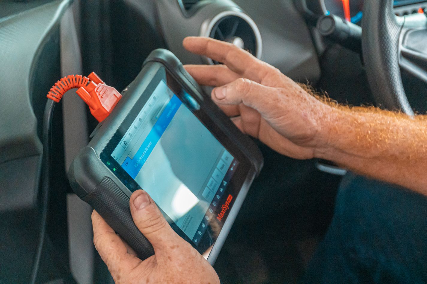 Mecânico usando tablet em veículo, representando indicadores e controle digital da oficina